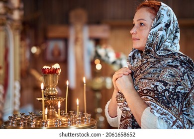 a young woman in a headscarf prays in an Orthodox church and puts candles in front of icons