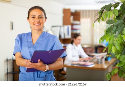 Young Woman Healthcare Worker In Blue Overall Posing In Medical Office