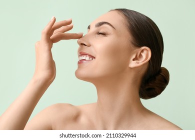 Young woman with healthy skin touching nose on color background