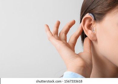 Young woman with hearing aid on light background