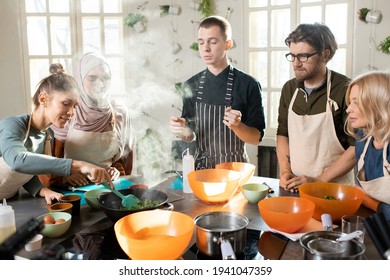 Young Woman With Heat Resistant Spatula Mixing Vegetables In Frying Pan While Standing By Electric Stove During Cooking Masterclass