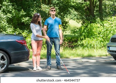 Young Woman Helping Blind Man Wearing Armband On Street