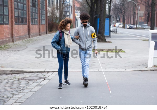 Young Woman Helping Blind Man With White Stick While\
Crossing Road