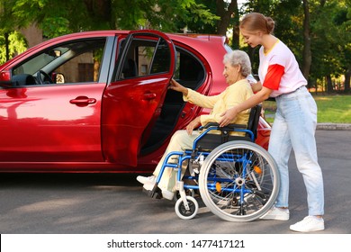 Young Woman Helping Disabled Grandmother In Wheelchair To Get Into Car Outdoors