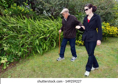 Young woman helping and supporting her grandfather to walk outdoor in the garden with his support walking stick.Real people. Copy space