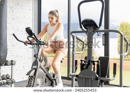 Young woman in her 20s using a stationary bike at the gym. Sport and health concept