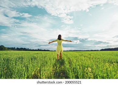 Young woman with her arms wide spread is enjoying in the sunny summer day, rear view
