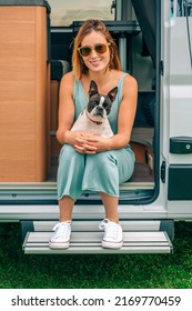 Young Woman And Her Boston Terrier Dog Looking At Camera Sitting At The Door Of Her Camper Van During A Trip