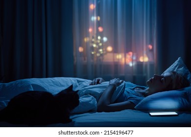 Young Woman And Her Cat Sleeping Cozily On A Bed In Bedroom At Night.