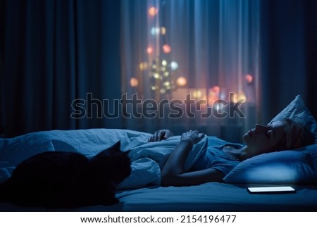 Young Woman And her Cat Sleeping Cozily on a Bed in Bedroom at Night.