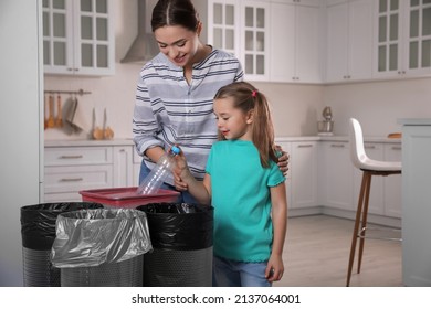 Young Woman And Her Daughter Throwing Plastic Bottle Into Trash Bin In Kitchen. Separate Waste Collection