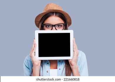 Young woman with her digital tablet. Young women holding her digital tablet in front of her face while standing against grey background - Powered by Shutterstock