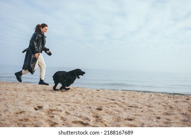 Young Woman And Her Dog Black Cocker Spaniel Running Along The Beach Having Fun