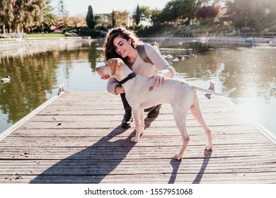 Young Woman And Her Dog Outdoors In A Park With A Lake. Sunny Day, Autumn Season