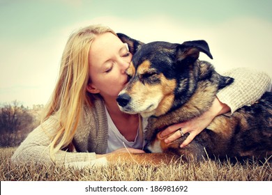 Young woman and her German Shepherd dog lying in the grass, she is hugging and kissing him. Vintage style color. - Powered by Shutterstock