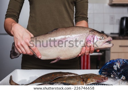 A young woman is in her kitchen with a box of fish and is holding a trout