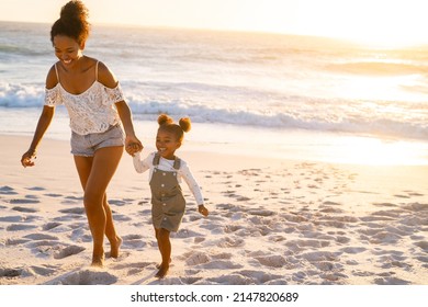 Young woman with her little cute girl running on beach during sunset. Cheerful and cute african american daughter walking and playing with mother on beach together. Bigger sister and child enjoying. - Shutterstock ID 2147820689