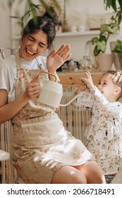 Young Woman And Her Little Daughter Is Watering Houseplants At Home And Having Fun Splashing Water.Home Gardening.Family Leisure,hobby Concept.Biophilia Design And Urban Jungle Concept.