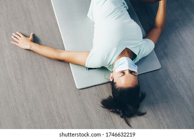 Young Woman With Her Mask On Is Lying Exhausted On Her Exercise Mat.