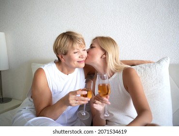 Young Woman With Her Mom Sitting On The Bed And Drinking Wine.