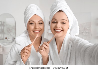 Young woman and her mother with toothbrushes taking selfie after shower in bathroom, closeup - Powered by Shutterstock