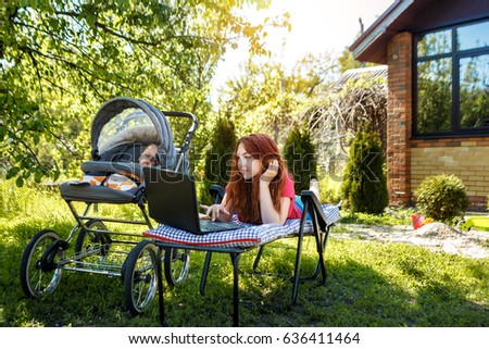 Young woman with her newborn baby lying on the grass in the park and enjoying sunny summer day. Mother with child outdoors. Motherhood.