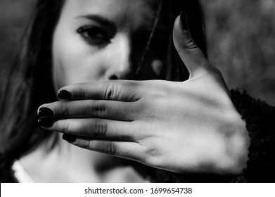 Young woman hiding her mouth with one hand. No freedom of speech, silence. Focus on the hand, black and white.