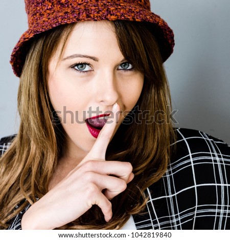 Young Woman Hiding A Secret Or Surprise With A Finger In Front Of Her Mouth Wearing A Red Woolen Hat with Her Mouth Open