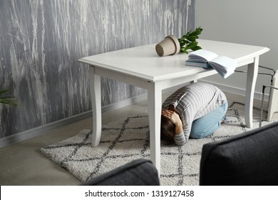 Young Woman Hiding Under Table During Earthquake