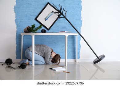 Young Woman Hiding Under Table During Earthquake