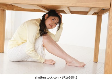 Young woman hiding under table from earthquake   