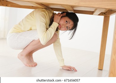 Young Woman Hiding Under Table From Earthquake   