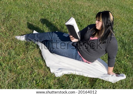 A young woman with highlighted hair reading a book or doing homework on campus.