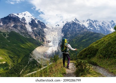 Young Woman Hiker From Behind With Backpack Hiking On Mountain Trail In Summer In Green Caucasus Mountains. Mountain Hike, Active Lifestyle, Travel Destination