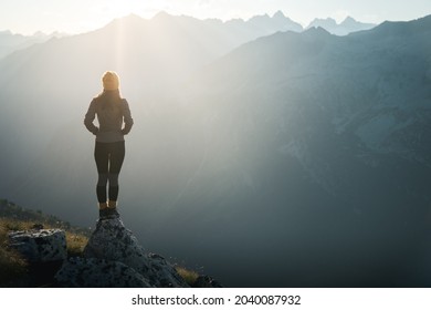 Young woman hiker standing on the edge of cliff at sunrise. Female tourist reaching summit enjoying amazing sunrise in the mountains.Backlight sunlight with beautiful lens flare and sunbeam.Copy Space - Powered by Shutterstock