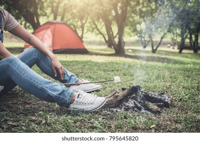 Young woman hiking cooking a marshmallow candies on the campfire in forest, hike and people concept - happy relaxation camping.