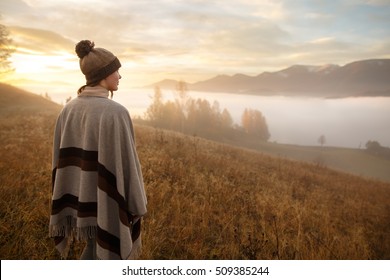 junge Frau wandern auf Berggipfel über Wolken und Nebel Hiker Mädchen Umhüllung in warmen Poncho Outdoor.Früher Morgen.Misty Berg.Junge Mädchen über den Wolken im Tal Blick auf ruhigen Herbstsonnenaufgang