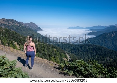 Young woman hiking on Hurricane Ridge trail in Olympic National Park, Washington observes cloud inversion on sunny autumn afternoon.