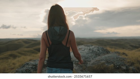 Young woman hiking at sunset on a hilltop, surrounded by rolling hills and dramatic sky - Powered by Shutterstock