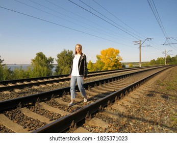 Eine junge Anhalter in einer Jacke und Jeans mit Rucksack auf der Eisenbahnstrecke bewundert die Aussicht auf die Bucht auf einem sonnigen Herbsttag