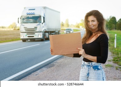 Young woman hitchhiker on the road is holding a blank cardboard sign 