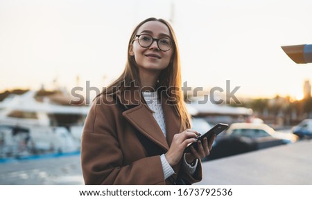 Young woman hold sellphone in evening port Barcelona. Girl in glasses using smartphone technology. Digital business communication
