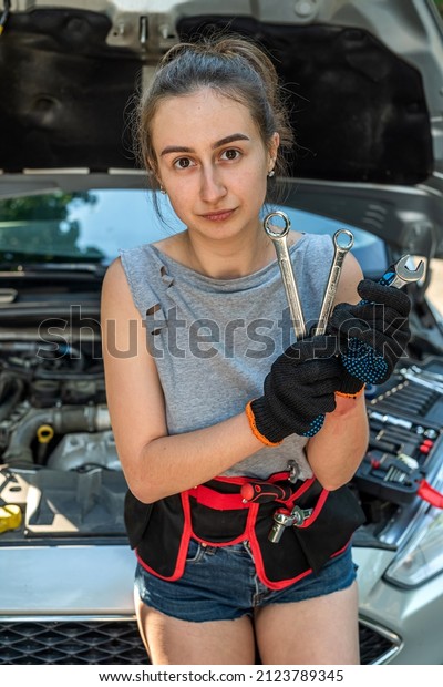 Young woman hold tools for repair and waiting\
for help near broken car. summer\
time