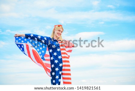 Young woman holding American flag on blue sky background, wearing in red, white and blue costume, celebrating United States of America Independence Day. Happy American patriot adult girl in a 4th of