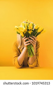 young woman holding beautiful yellow tulips and daffodils on yellow Stock Photo