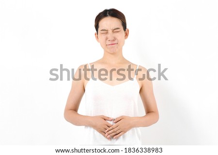 Young woman holding a belly suffering from abdominal pain wearing a white camisole on a white background