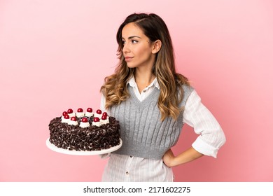 Young Woman Holding Birthday Cake Over Isolated Pink Background Looking To The Side