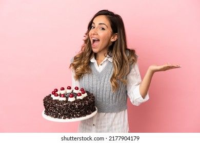 Young Woman Holding Birthday Cake Over Isolated Pink Background With Shocked Facial Expression