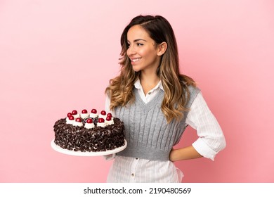 Young Woman Holding Birthday Cake Over Isolated Pink Background Looking To The Side And Smiling