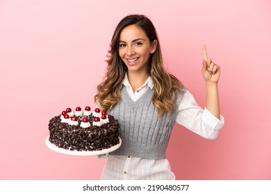 Young Woman Holding Birthday Cake Over Isolated Pink Background Pointing Up A Great Idea